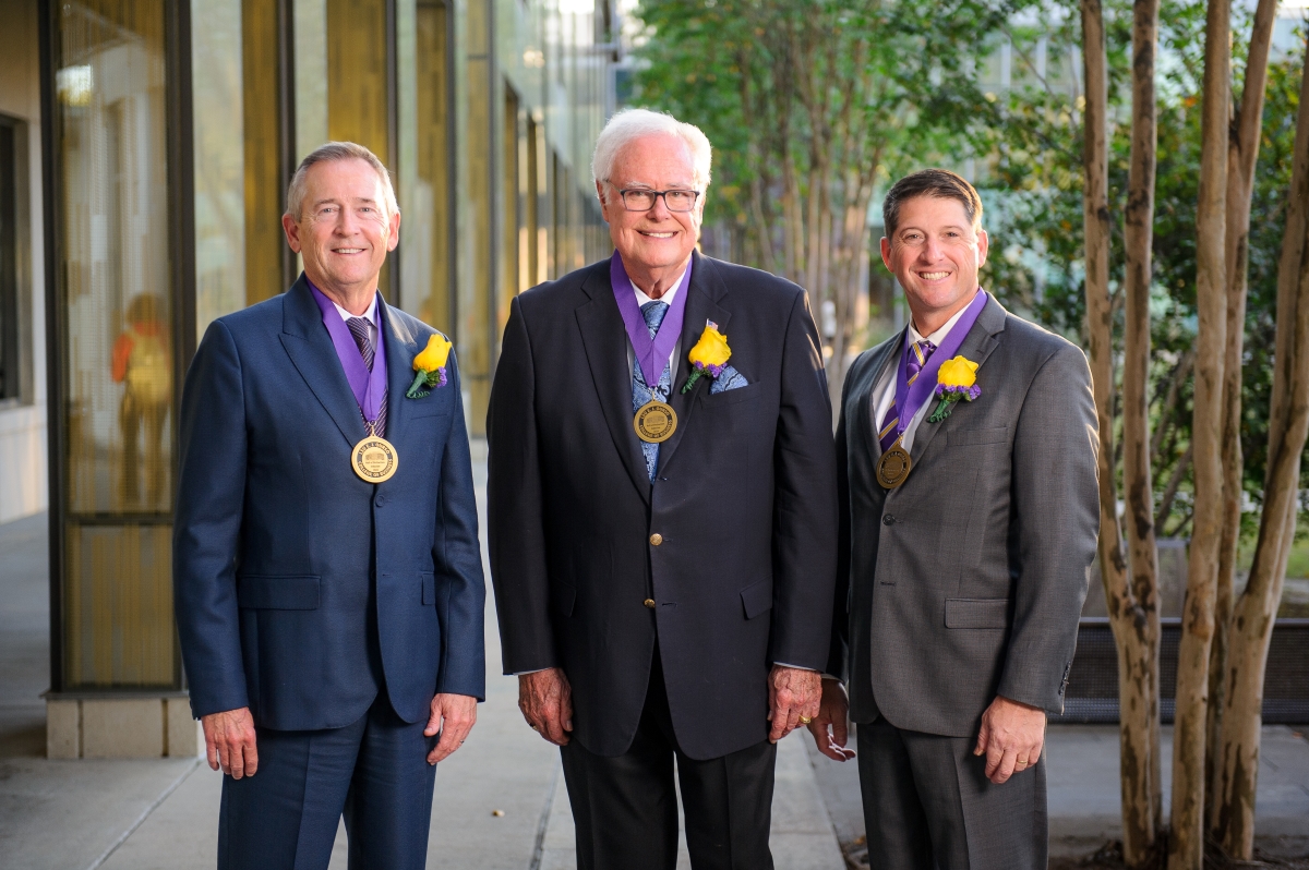 Three men in suits wearing medals around their necks. They are standing side by side and smiling. 