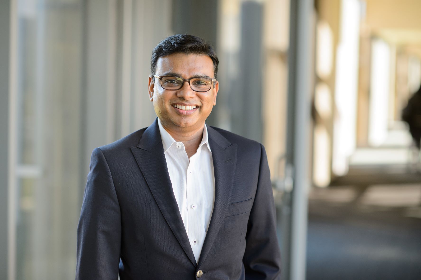 Rajesh Narayanan wears a suit and stands in a sunny hallway in the BEC.