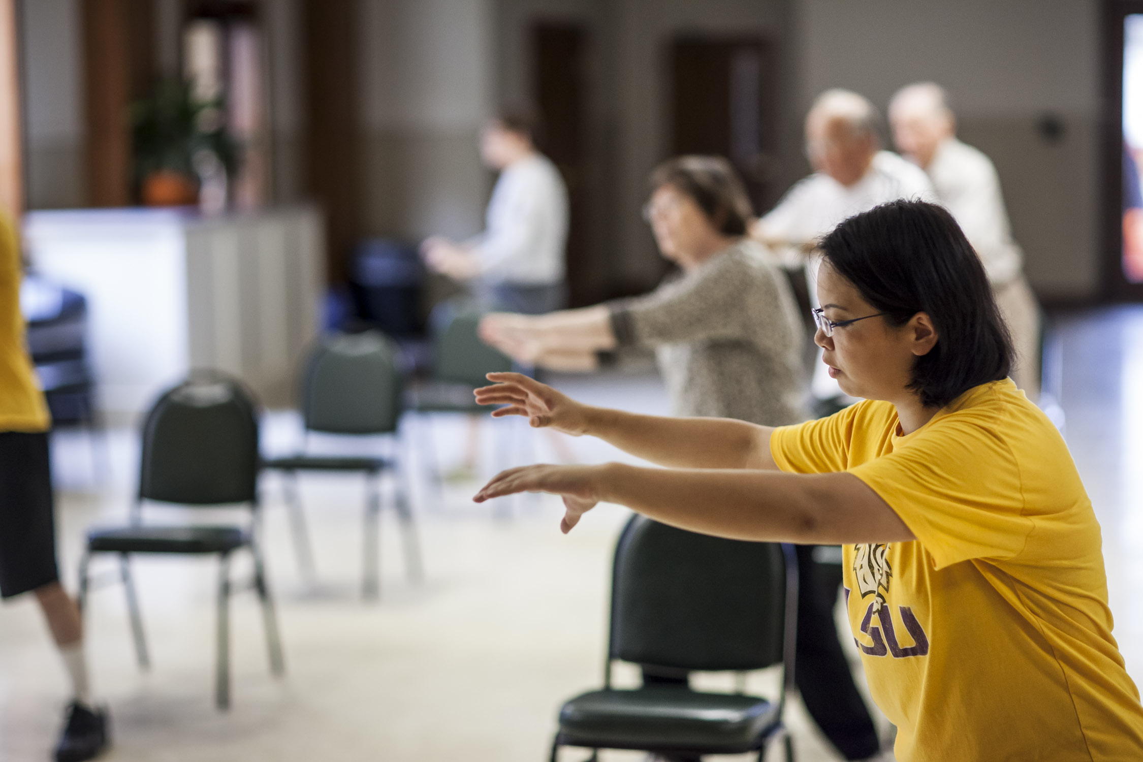 female doing Tai Chi with other adults in background