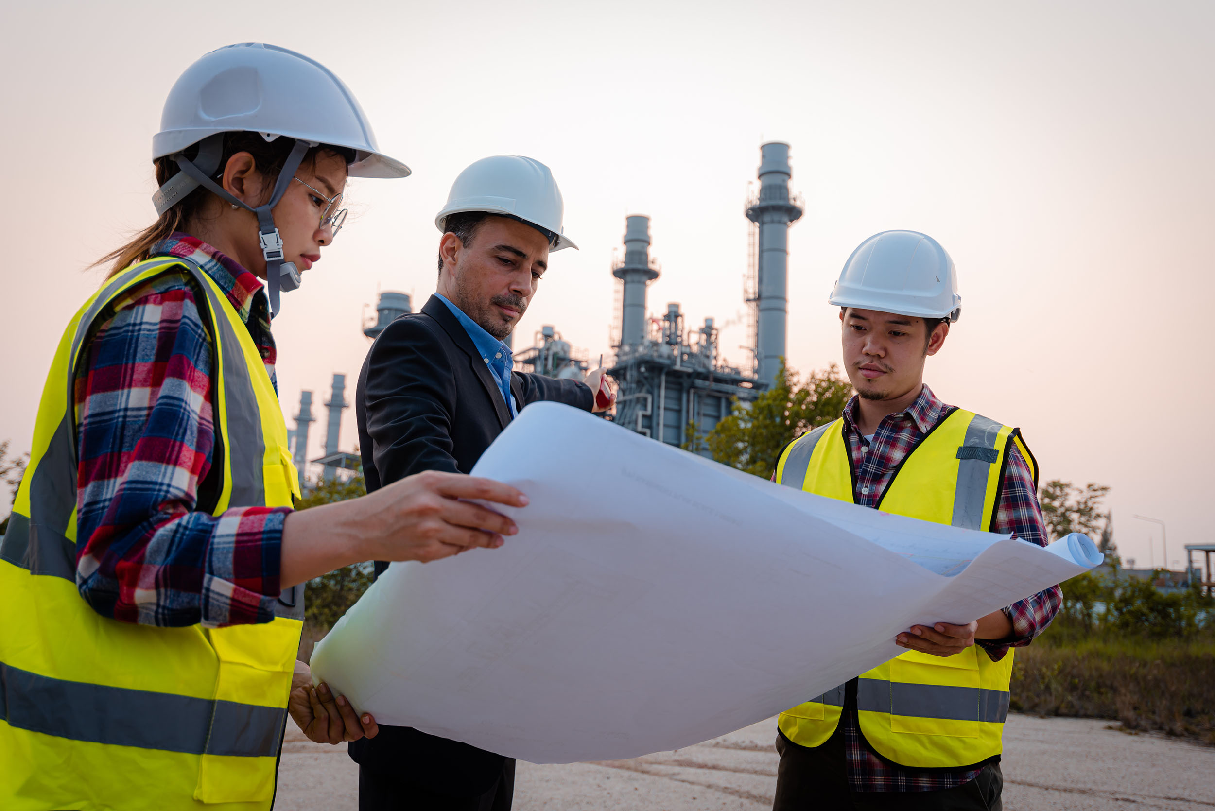 plant workers in neon vests and hardhats looking at blueprints