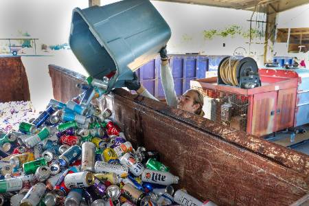 A young man pouring a bin of bottles and cans into a roll off dumpster.